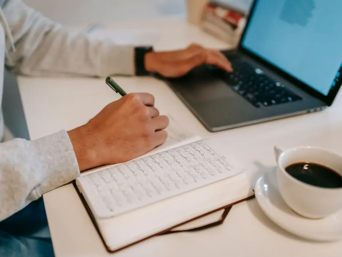 Copywriter drafting notes next to a laptop and coffee