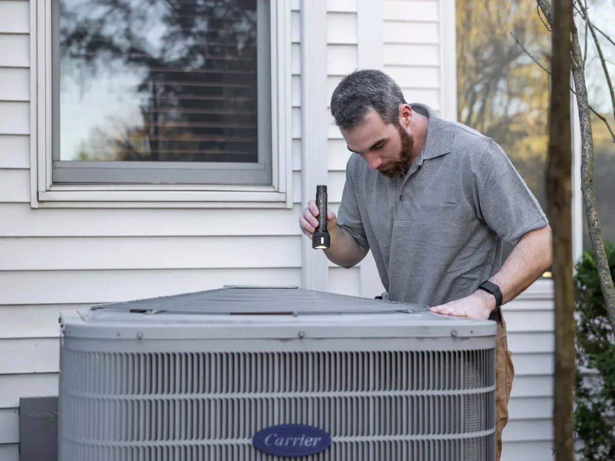 HVAC technician inspecting an outdoor air conditioner beside a house