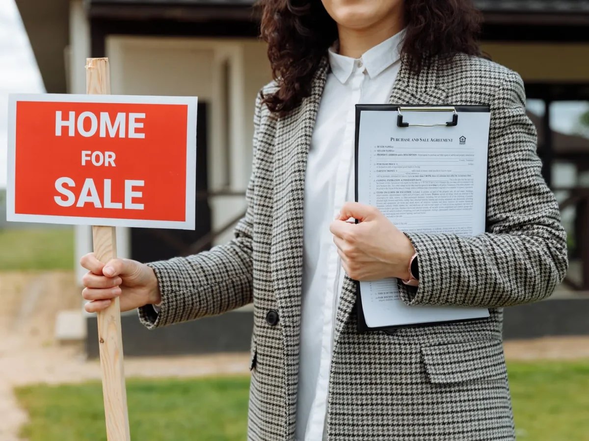 Real estate agent holding a home for sale sign