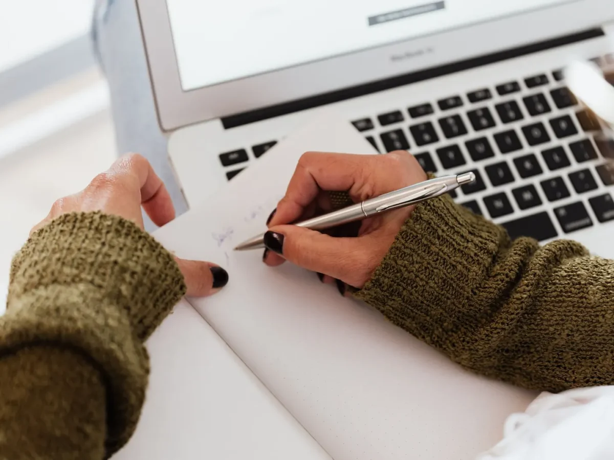Writer taking notes beside a laptop